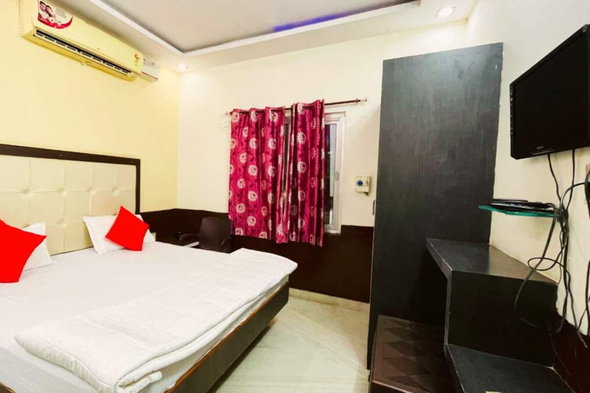 A hotel room with a bed, a TV, an air conditioning unit, and a curtain.