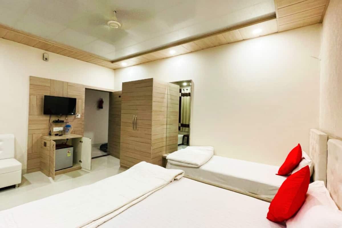 A hotel room with a white sofa, a bed with red pillows, a TV mounted on the wall, and a wardrobe.
