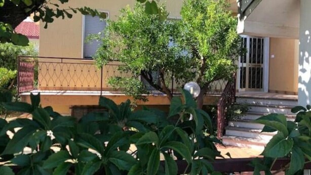 Ein Wohngebäude mit Balkon, einem kleinen Baum und einem Metallzaun.