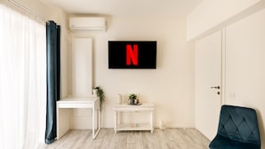 A modern room with a white desk, a white console table with a plant, a blue chair, and a wall-mounted TV displaying a red 'N'. - Metropole Apartments Ateneum Residence (Bucharest)