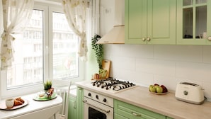 A kitchen with green cabinets, a gas stove, a toaster, and a window with curtains. - Metropole Apartments Ateneum Residence (Bucharest)