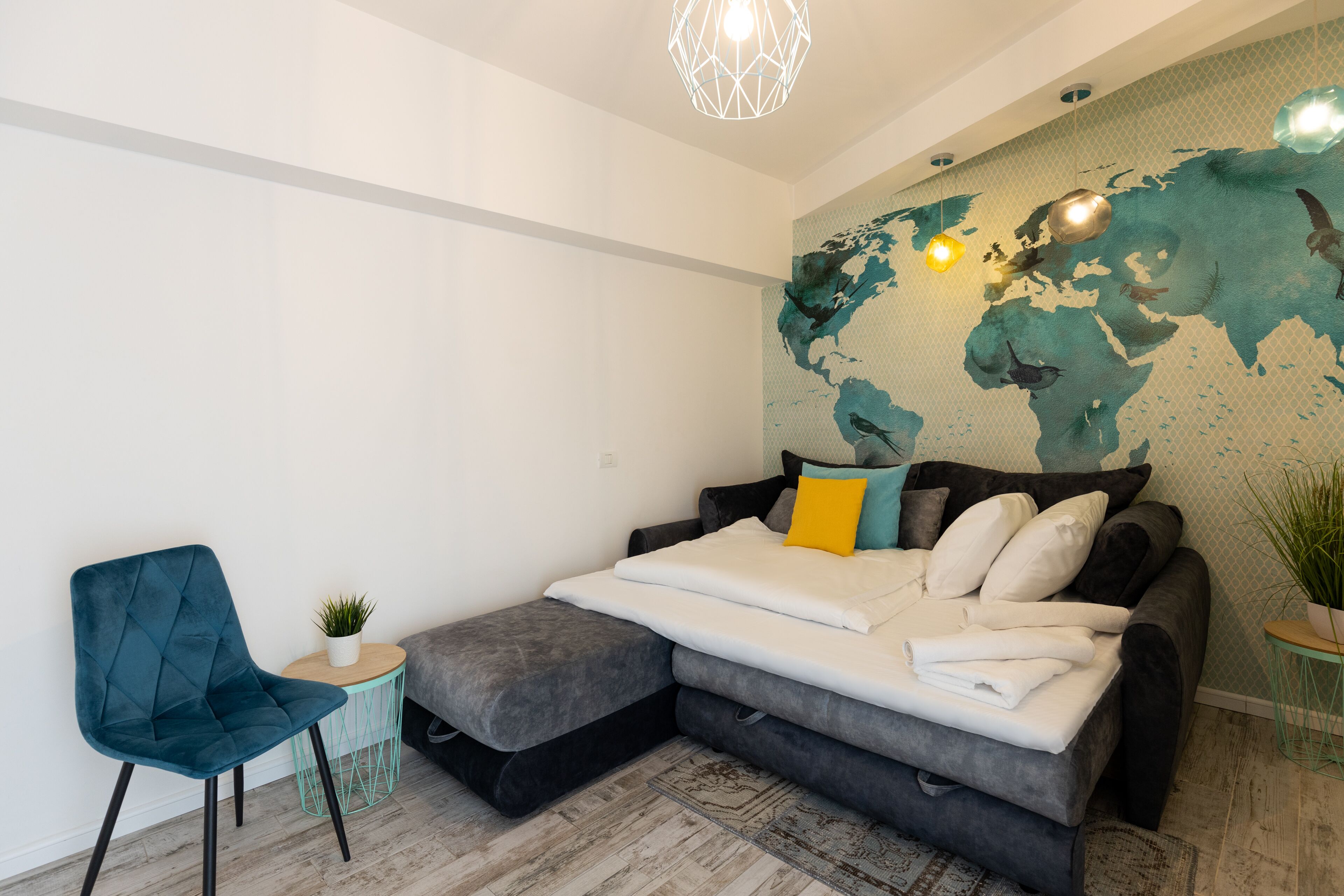 Een moderne slaapkamer met een bed, een stoel, een klein tafeltje en een muurschildering van een wereldkaart.