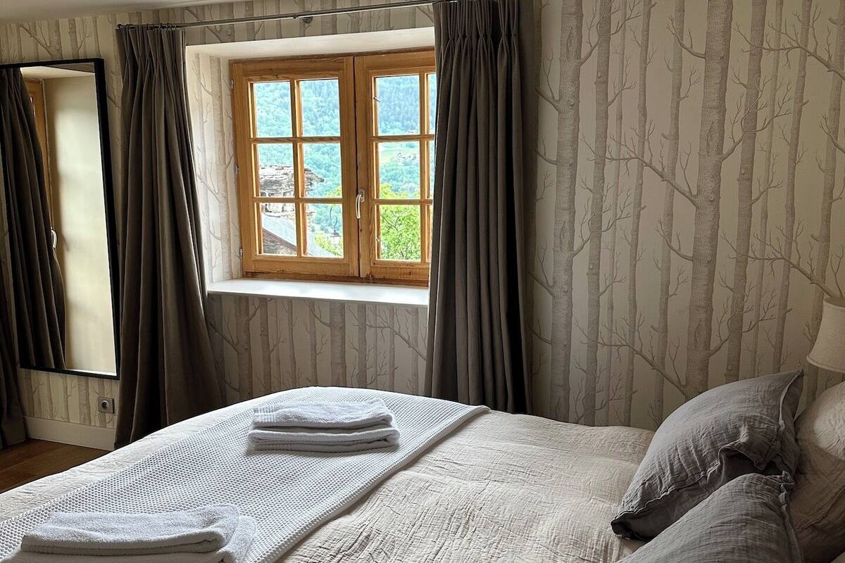 A bedroom with a large bed, a window with curtains, and a view of trees outside.
