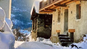 Una chaleta tradicional con balcones de madera y una torre de campanas, rodeada de nieve y montañas.