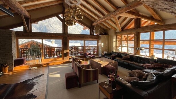 Amplia sala de estar con techo alto, vigas de madera y grandes ventanas con vistas a la montaña.