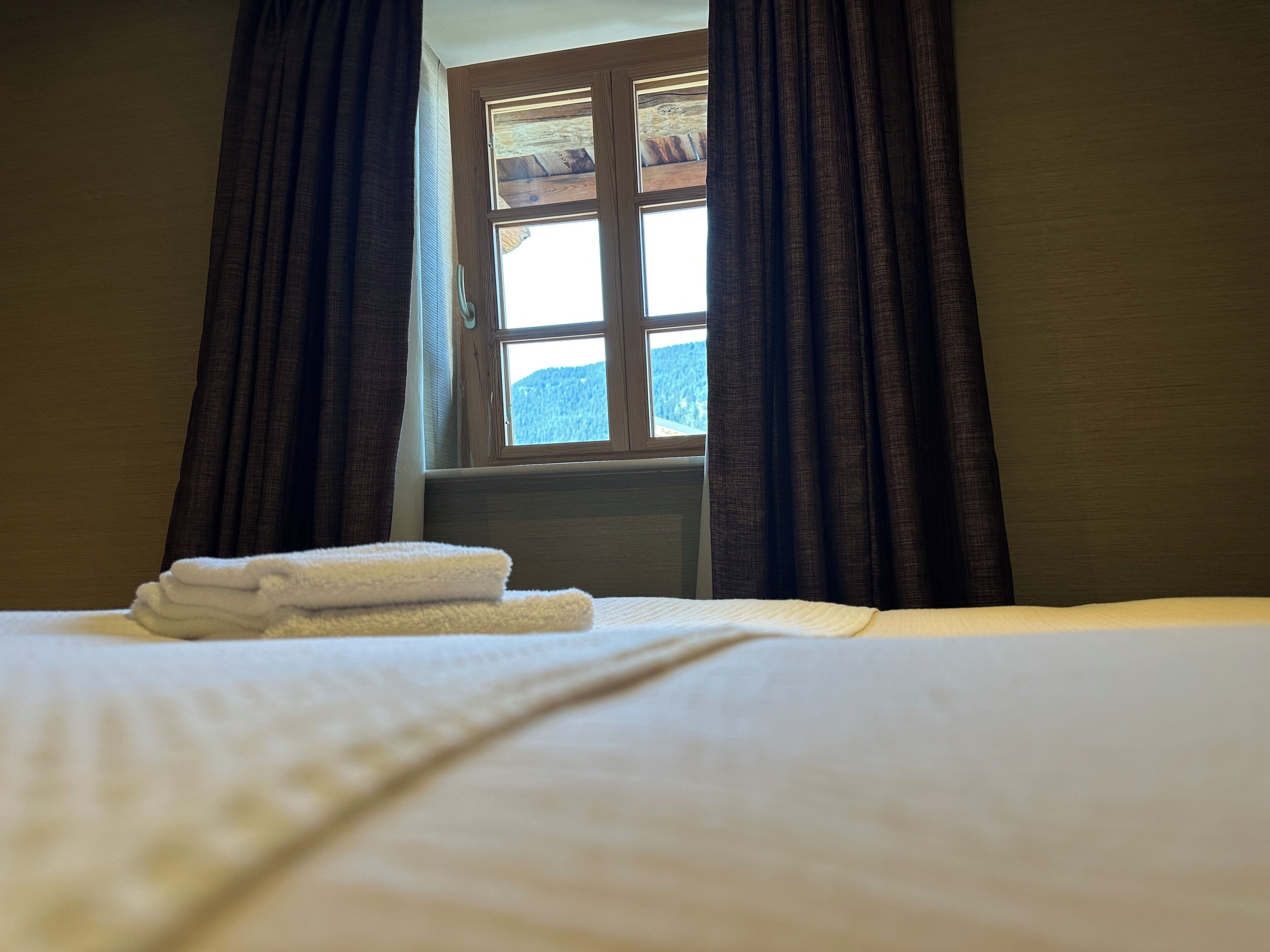 Une chambre d’hôtel avec un lit, une fenêtre avec des rideaux et une vue sur une montagne.