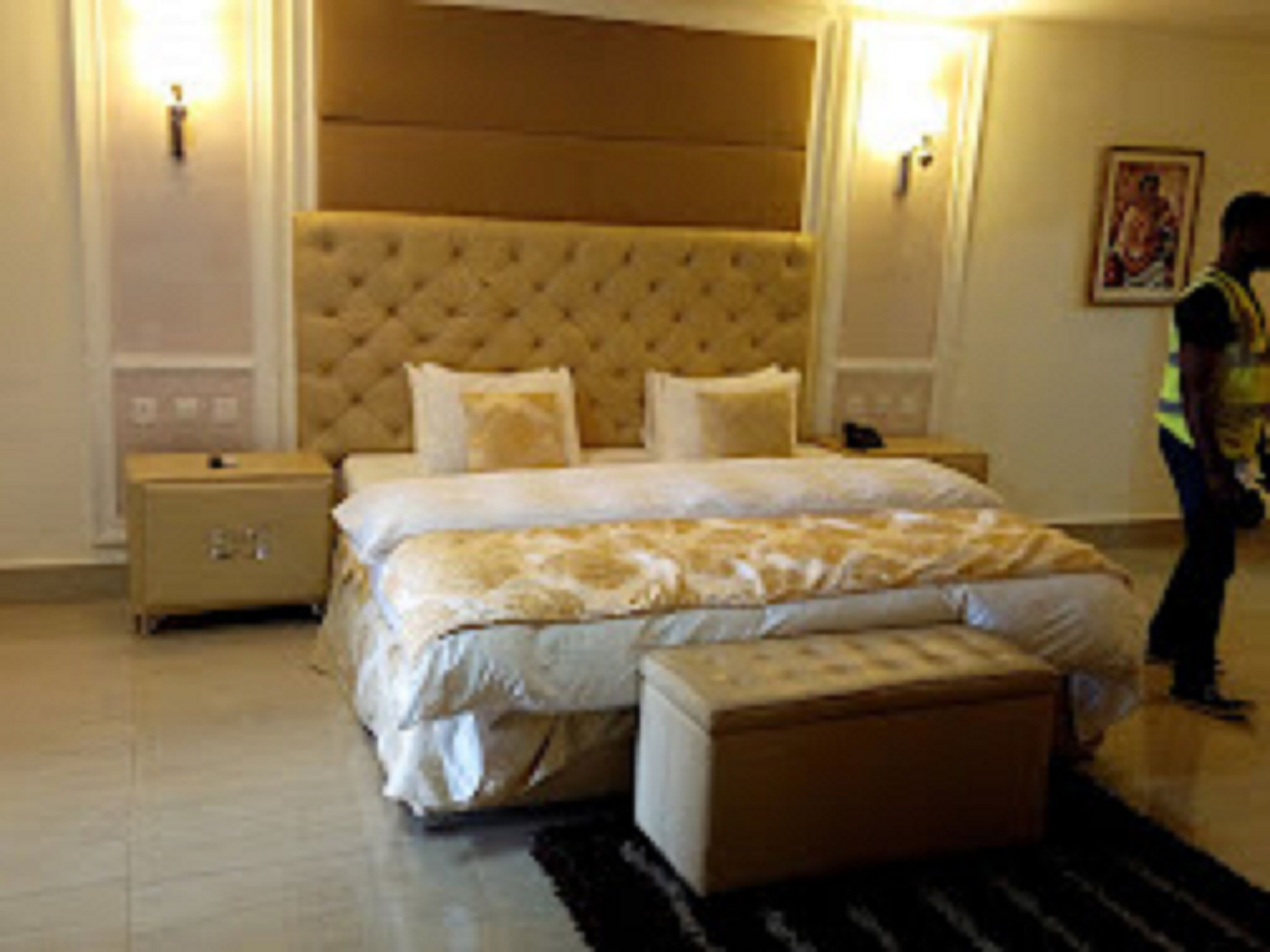 Une chambre d’hôtel avec un grand lit, une table de chevet, un banc et un luminaire fixé au mur.