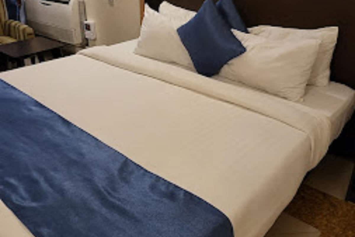 A hotel room with a large bed, a wooden headboard, and a bedside table with a lamp.
