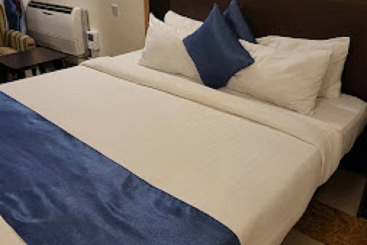 A hotel room with a bed, a nightstand, a wall-mounted heater, and a framed picture.
