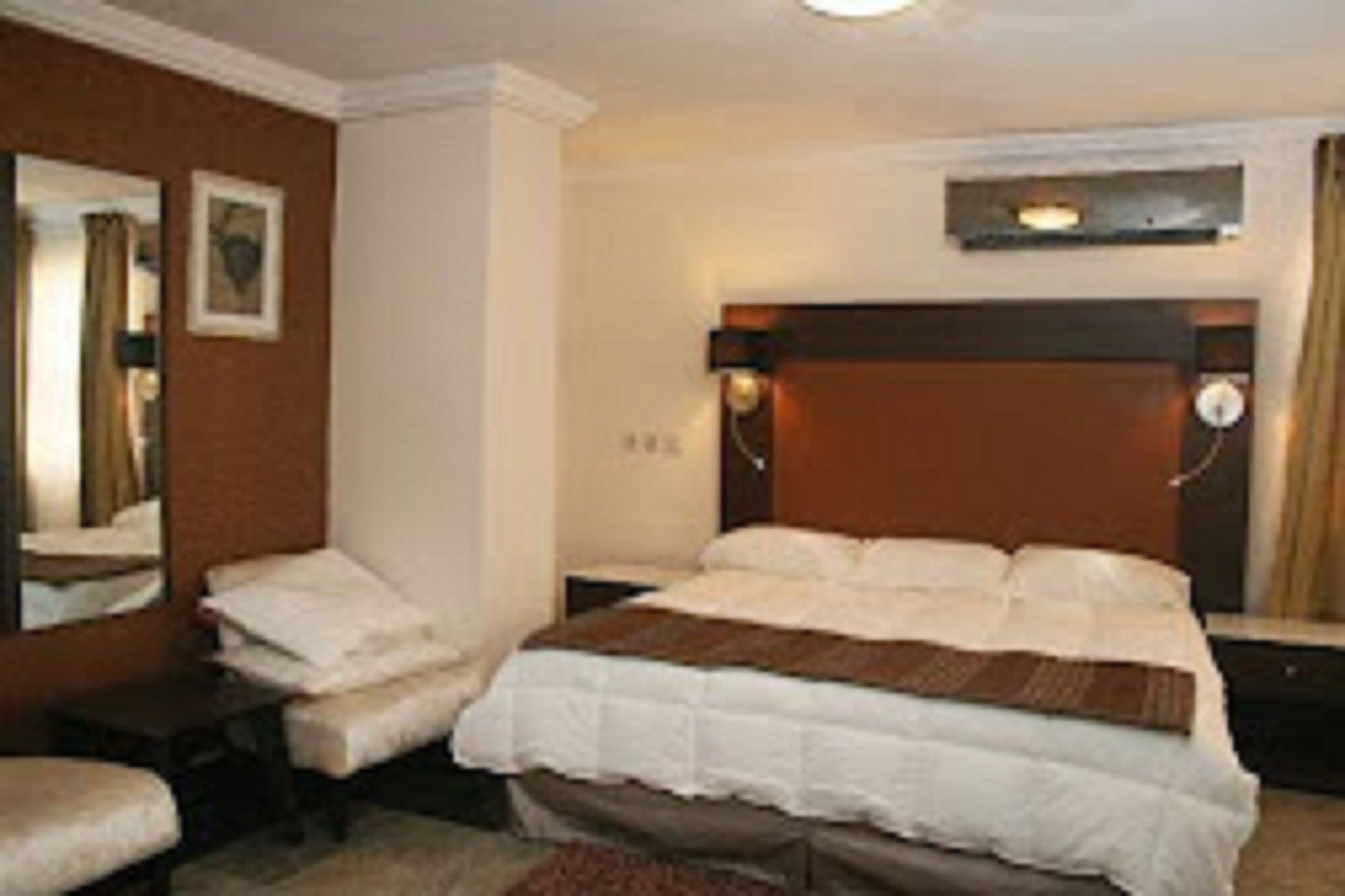 Een hotelkamer met een bed, nachtkastje, stoel en spiegel.