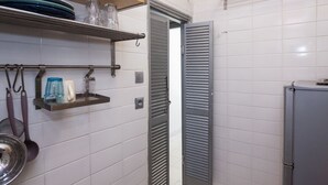 A kitchen with white tiled walls, a metal shelf with kitchenware, and a grey cabinet.