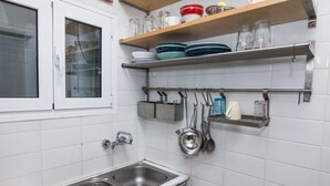 A kitchen with white tiled walls, a stainless steel sink, and shelves holding dishes and kitchen utensils.