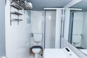 A modern bathroom with white tiles, a toilet, a bidet, a shower with a glass door, and a large mirror.