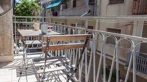 A balcony with a wooden chair and metal railings, overlooking a residential area with buildings and balconies.