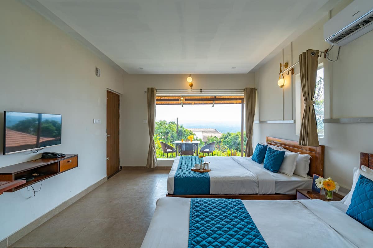 A hotel room with two beds, a TV, a desk with a chair, and a view of the outdoors.