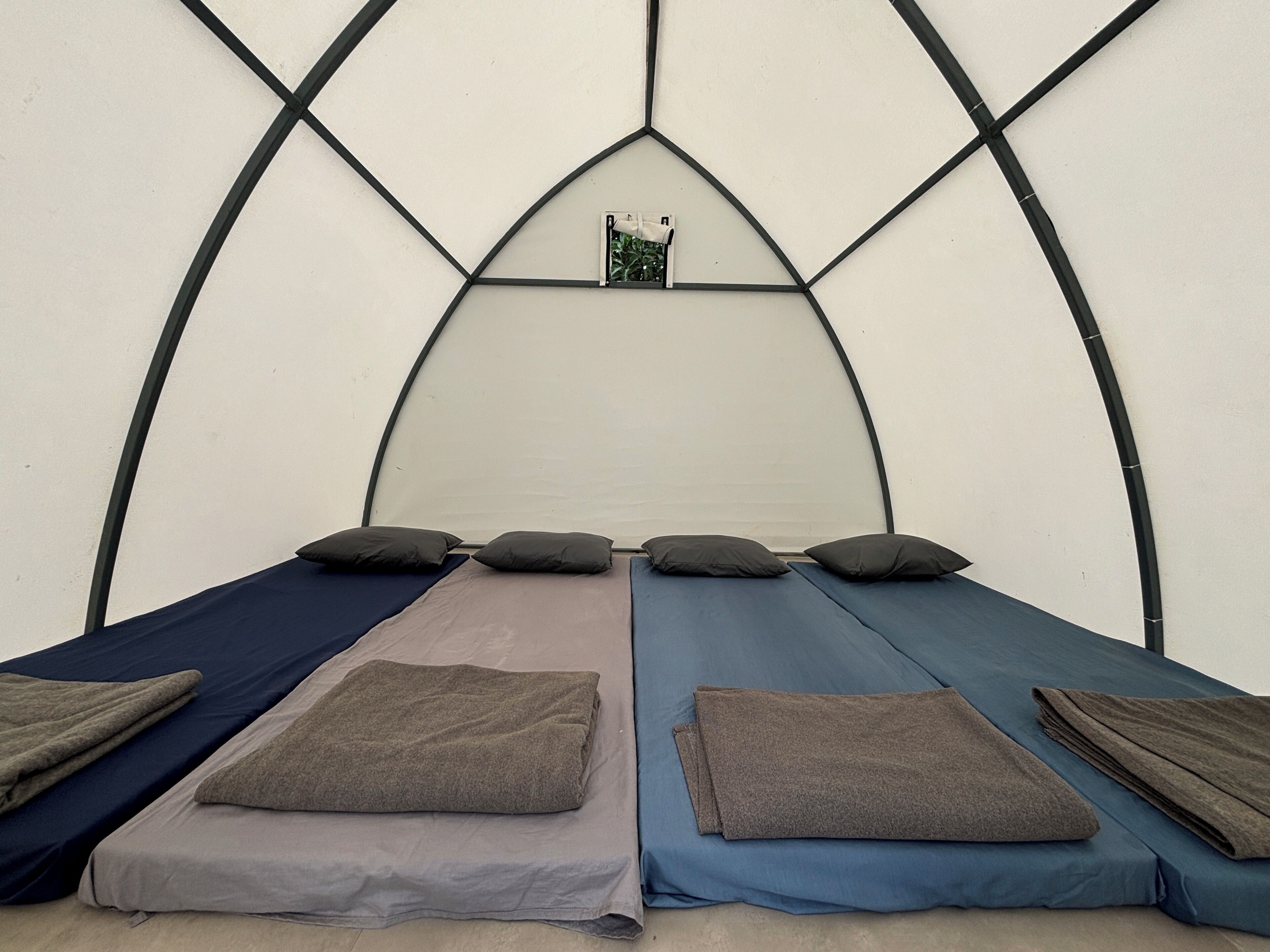 A tent-like room with four beds, each with a pillow and a folded blanket.