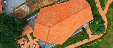 An aerial view of a building with a large orange roof, surrounded by greenery and a paved area with seating.