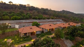 A resort with multiple bungalow-style buildings, each with a tiled roof and a small porch. The resort is surrounded by lush greenery and hills in the background.