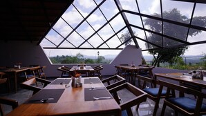 A restaurant with a geometric glass roof, wooden tables, and chairs, and a view of the landscape. - Ravishing Retreat  (Ramanagara)