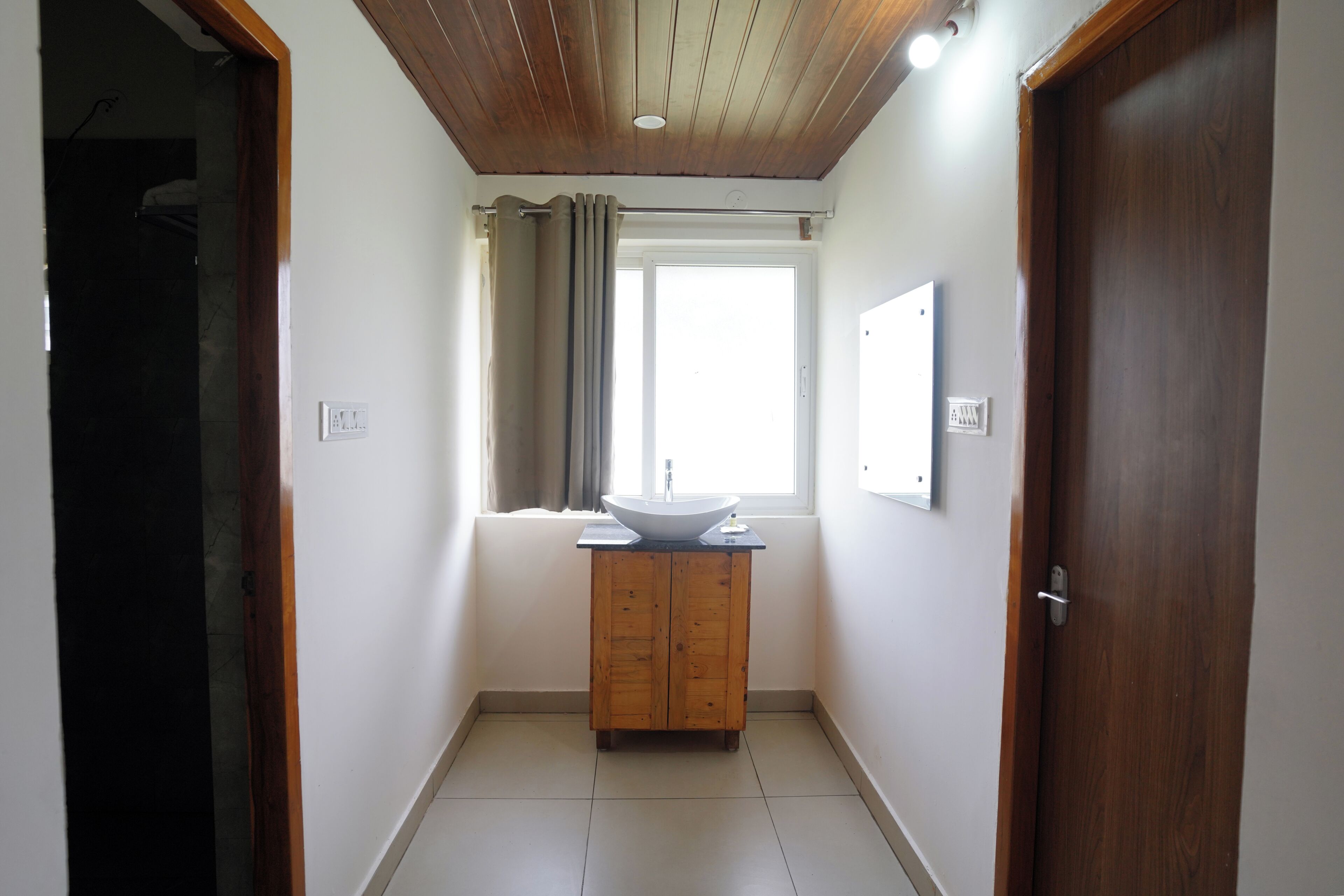 A hallway with a wooden door, a window with curtains, and a sink with a mirror.