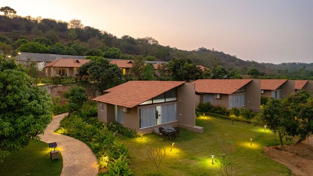 A row of modern, single-story buildings with red-tiled roofs, surrounded by lush greenery and a winding pathway. - Ravishing Retreat  (Ramanagara)