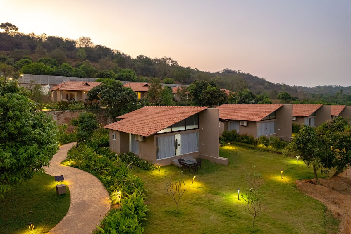A row of modern, single-story buildings with red-tiled roofs, surrounded by lush greenery and a winding pathway.