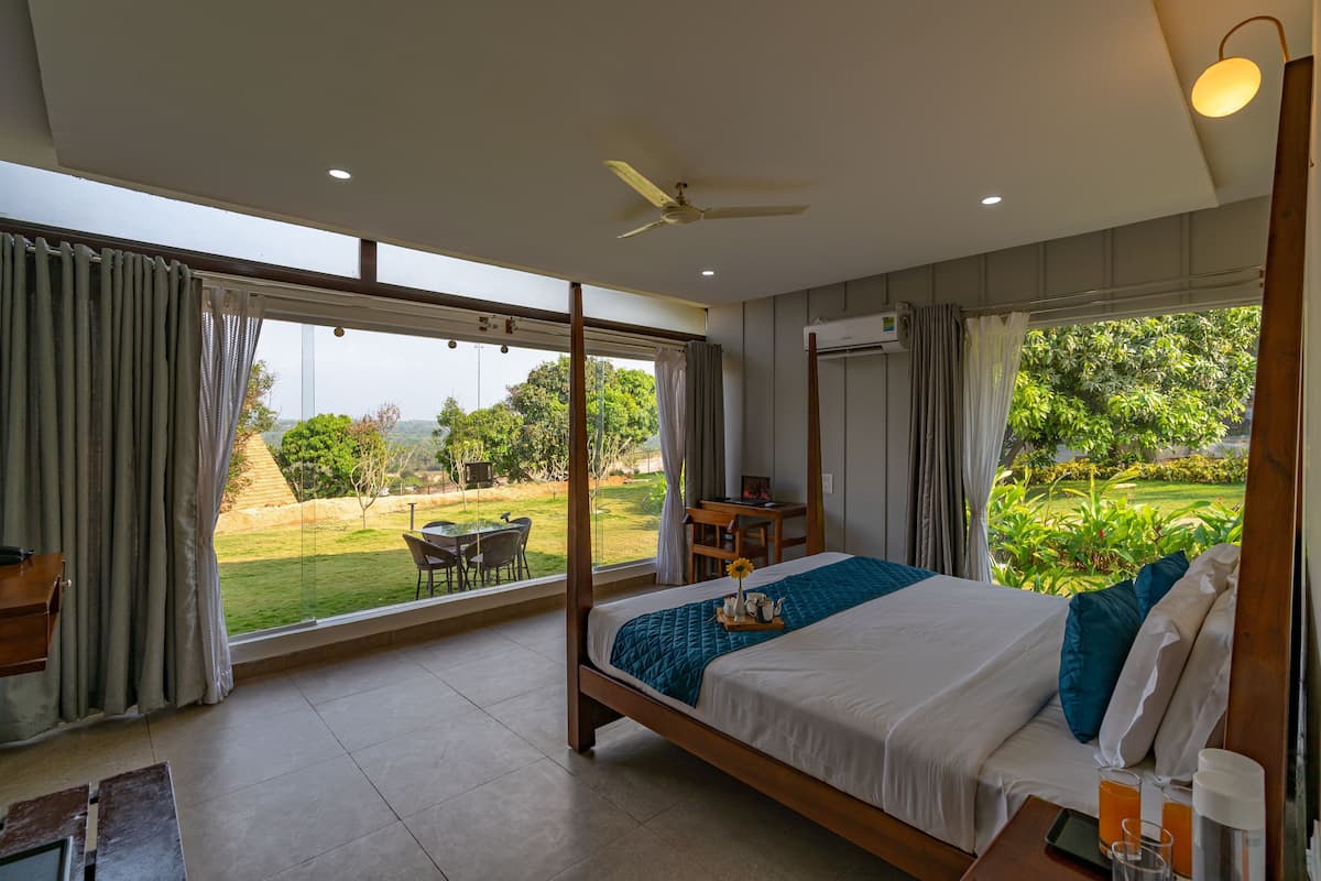 A bedroom with a large bed, a desk, and a view of a garden.