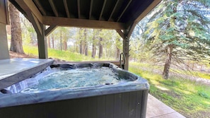 A hot tub under a wooden pergola with a forest view. - Mackinaw Minnow - Payette Lake Views - Downtown McCall Apt- Walk to Lake, Restaurants, Bars, Marina (McCall)