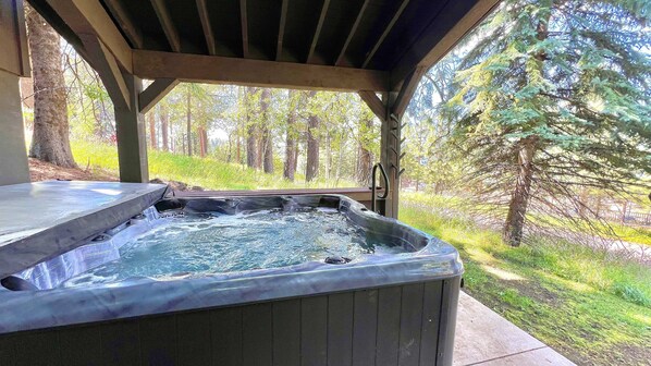 A hot tub under a wooden pergola with a forest view.
