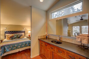 A bedroom with a large bed, a nightstand, a dresser, and a bathroom with a sink and mirror.