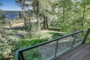 A deck with a view of a landscaped area, including a lawn and trees, overlooking a body of water and distant buildings.