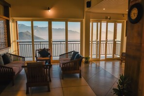 A room with a large sliding glass door leading to a balcony with a view of mountains. There are wooden chairs and a small table in the room. - Chill Berg Resort - Bodimettu (Bodinayakanur)