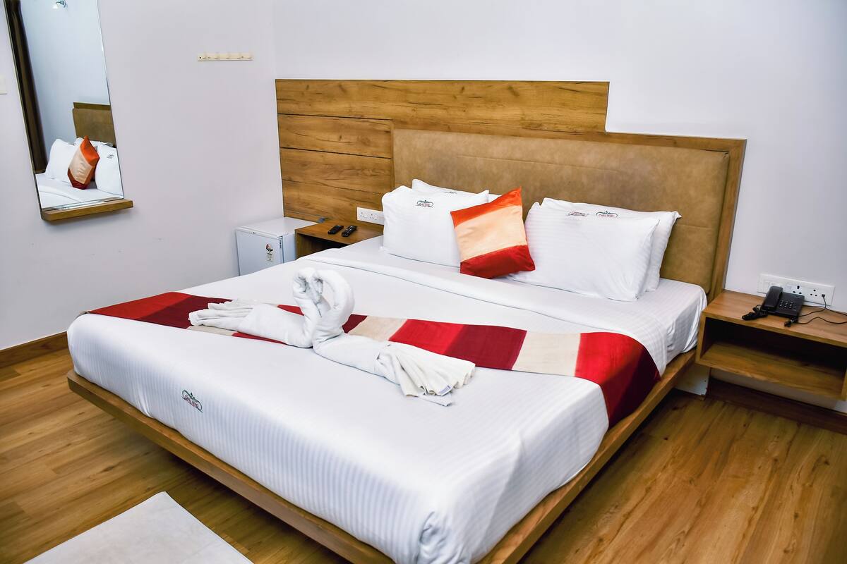 A hotel room with a wooden headboard, two beds, a bedside table with a phone, and a mirror on the wall.