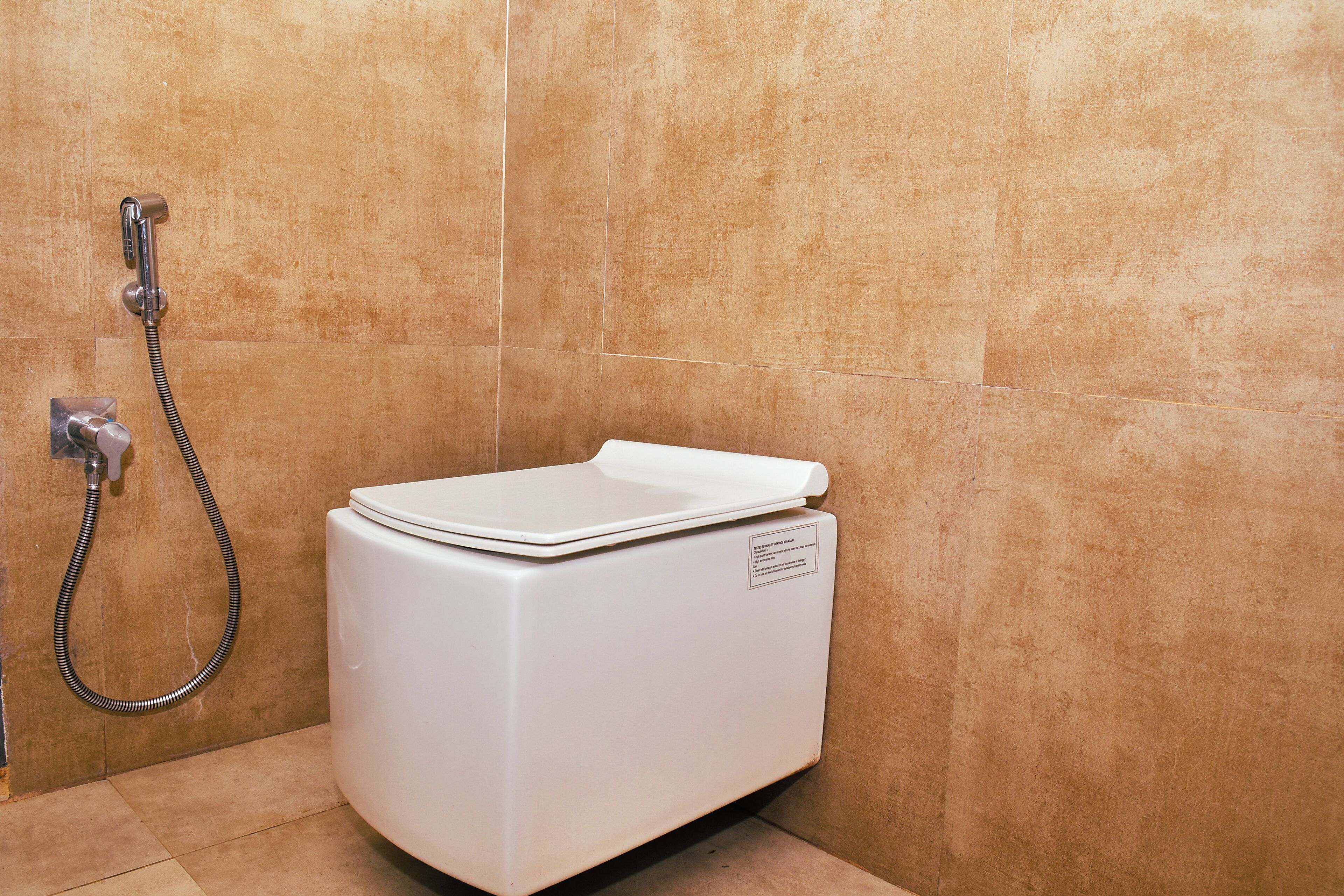 Een wit toilet met bedieningspaneel en douchekop in een badkamer met beige betegelde wanden.