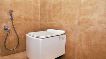 Een wit toilet met bedieningspaneel en douchekop in een badkamer met beige betegelde wanden.