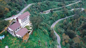 A large, multi-story building with a red roof, surrounded by lush greenery and winding roads. - Chill Berg Resort - Bodimettu (Bodinayakanur)