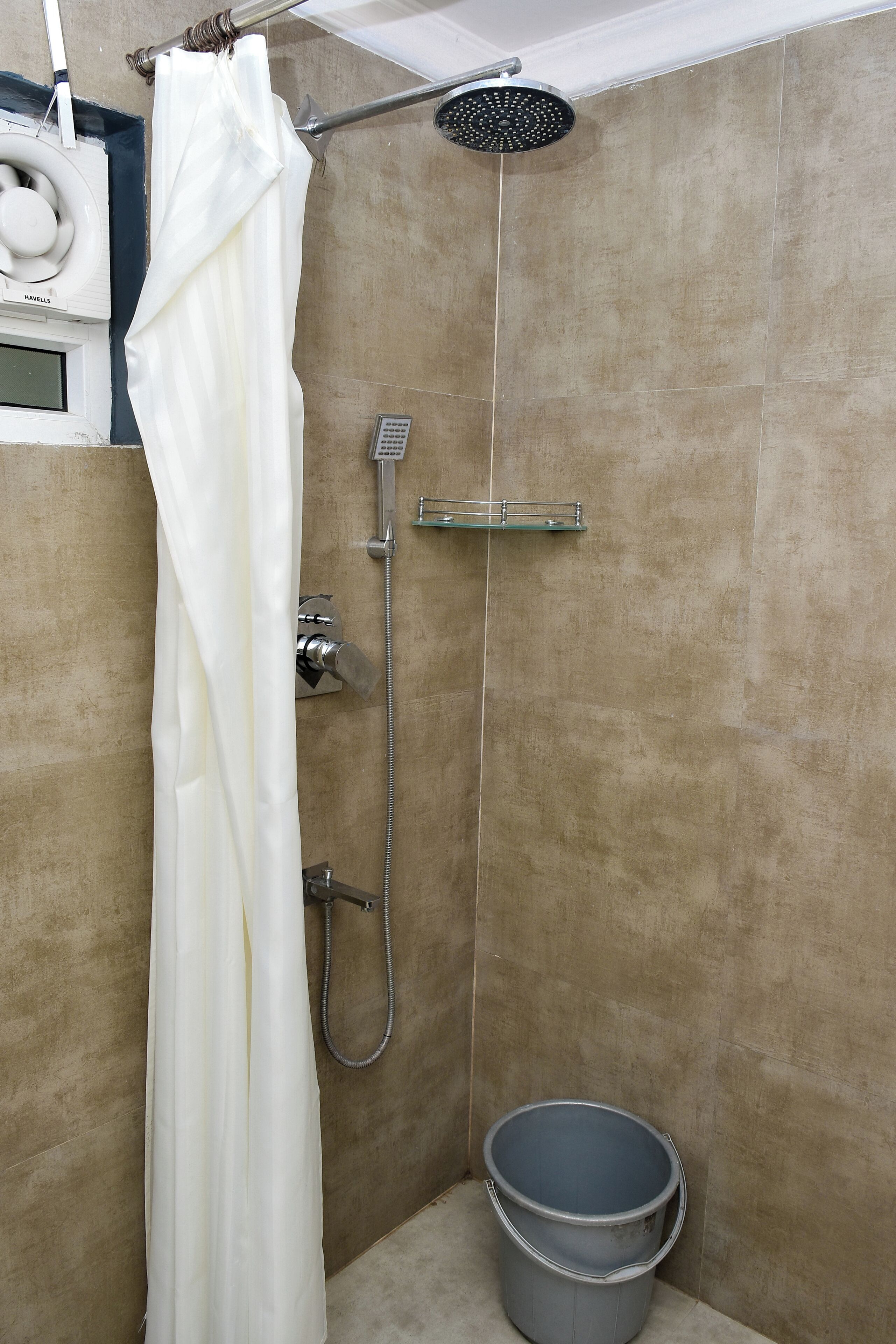 Ducha con cortina blanca, cabezal de ducha manual, estante fijado a la pared y un cubo.