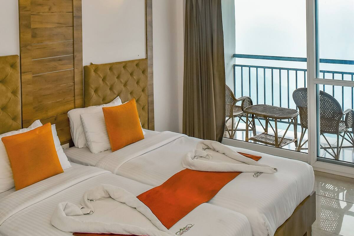 A hotel room with two beds, a wooden headboard, a balcony with wicker furniture, and a view of the sea.