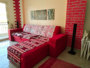 Un canapé rouge agrémenté de plaids à motifs, un sol carrelé et un mur en briques orné d’œuvres d’art.