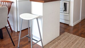 A compact kitchen with a microwave, toaster, and stove. There is a small island with a stool, and a chair is visible to the left. - 2ndhomes Cozy Apartment with Park View (Helsinki)