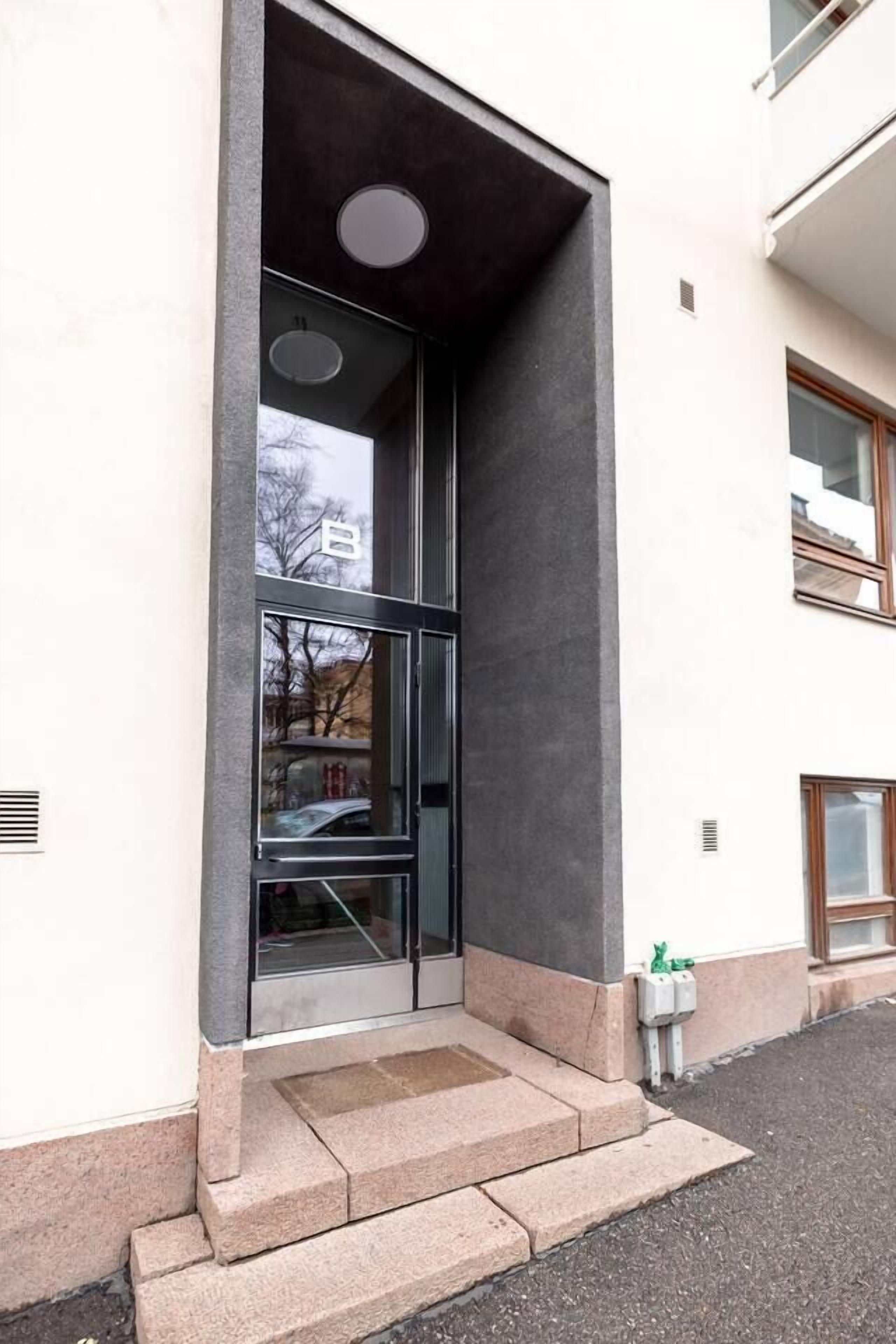 Une entrée d’immeuble avec une porte en verre, une structure en béton et une petite marche menant à la porte.