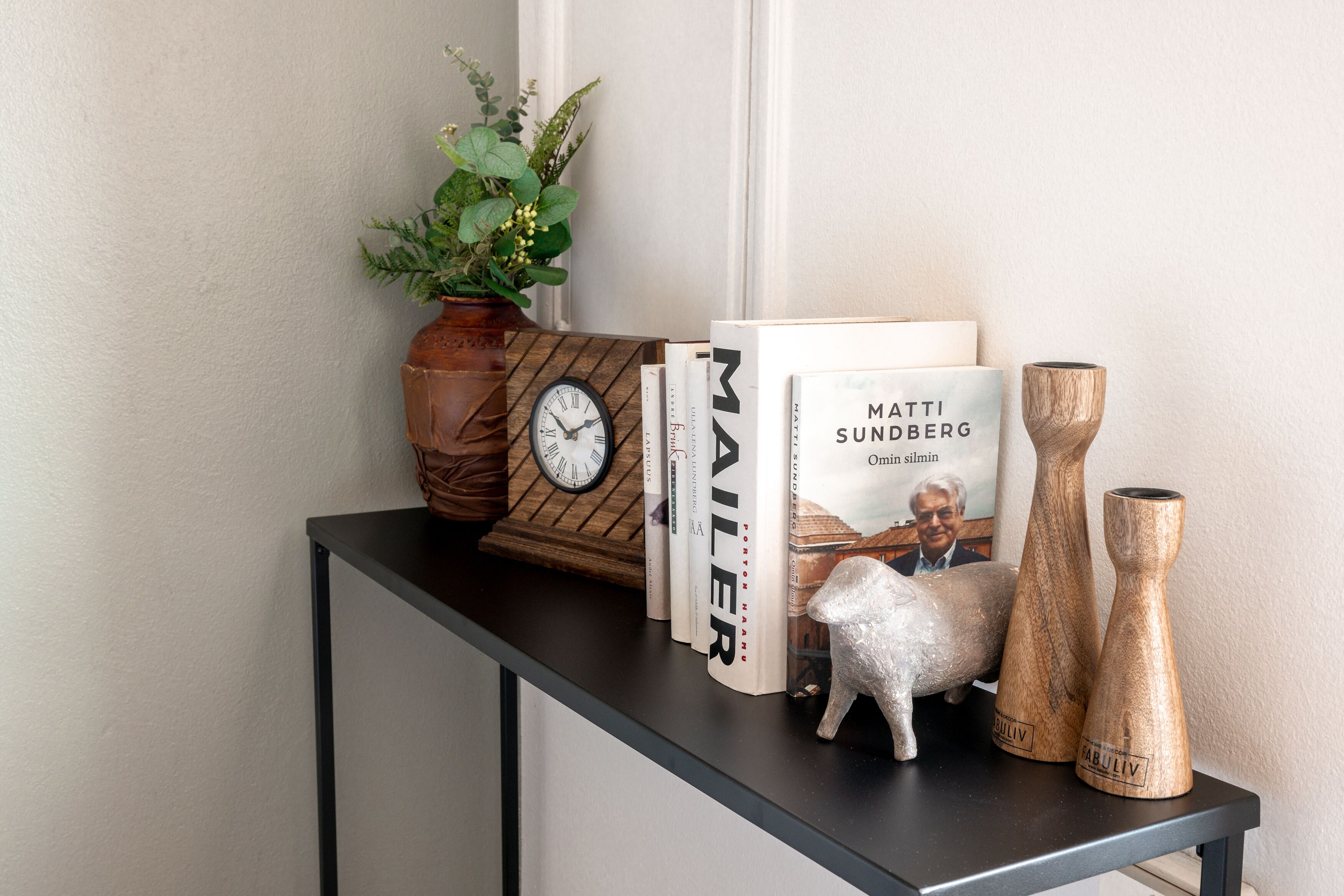 A console table with a clock, books, a decorative sheep, and wooden vases.