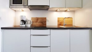 Una cocina moderna con armarios blancos, microondas de acero inoxidable, cafetera y protector de fregadero de madera.