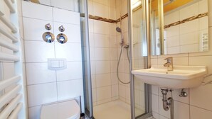 Un baño moderno con inodoro blanco, ducha con mampara de vidrio, lavabo y espejo.