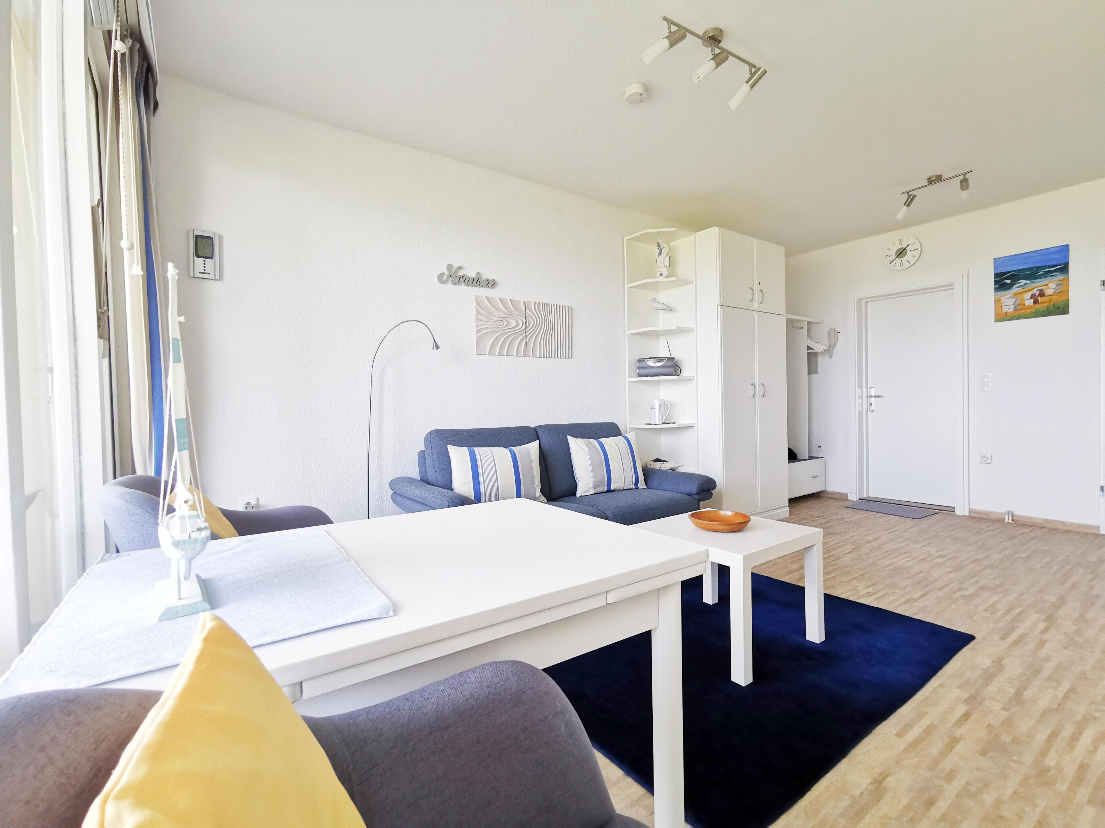 Ein modernes Wohnzimmer mit einer Couch, einem Couchtisch und einem Fernseher. Im Hintergrund befinden sich ein Kleiderschrank und eine Tür.