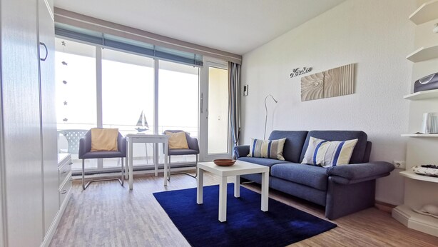 Una sala moderna con un sofá, dos sillones, una mesa de centro y un balcón con un modelo de velero.