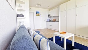 Una sala de estar moderna con un sofá, una mesita con un cuenco, y una cocina con armarios y un microondas.