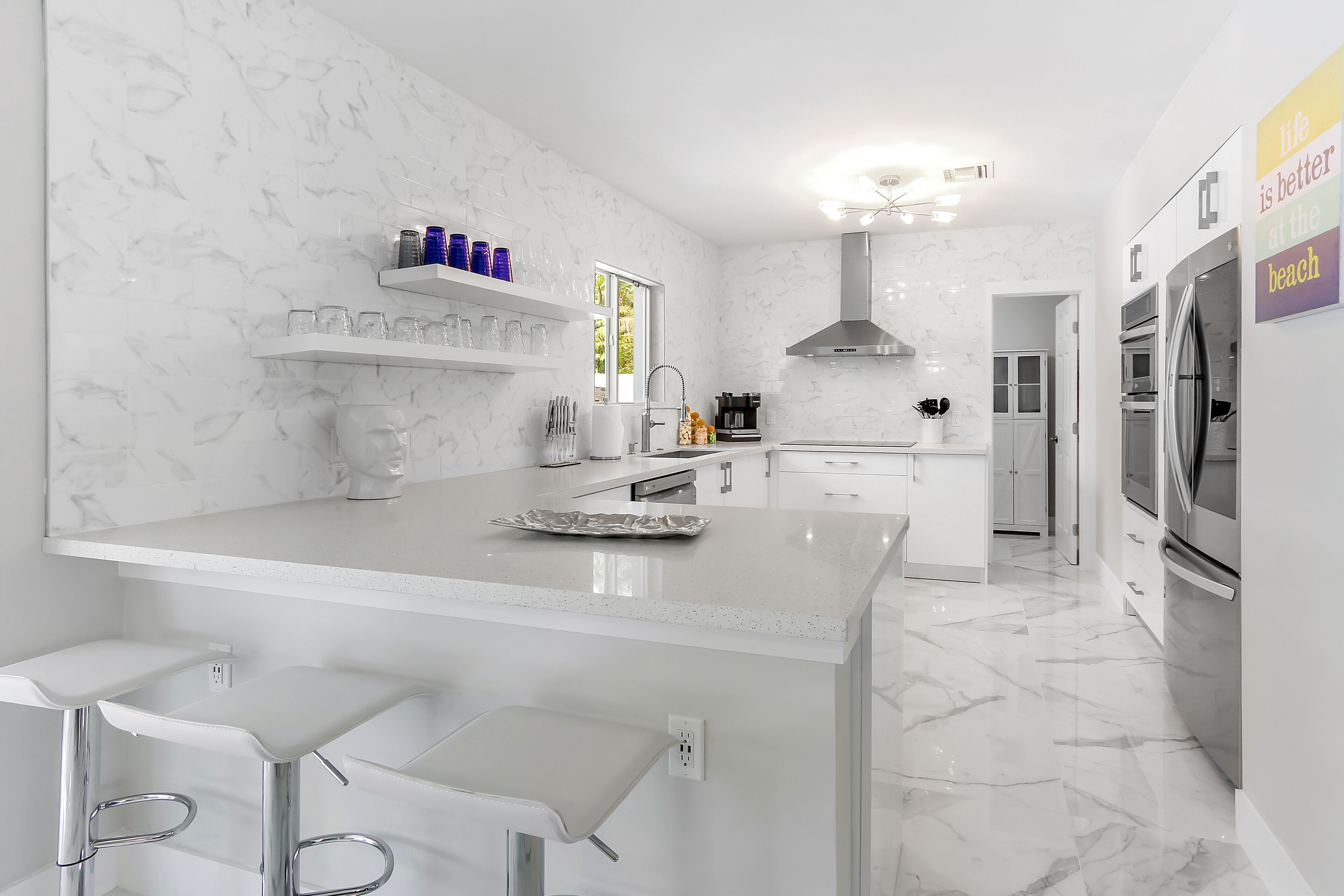 Una cocina moderna con encimeras de mármol blanco, electrodomésticos de acero inoxidable y una isla central con taburetes de bar.
