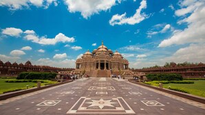 A large temple with a central dome and multiple smaller domes, surrounded by a well-maintained garden and a paved walkway leading to the entrance. - Hotel Vanson Delite (New Delhi)