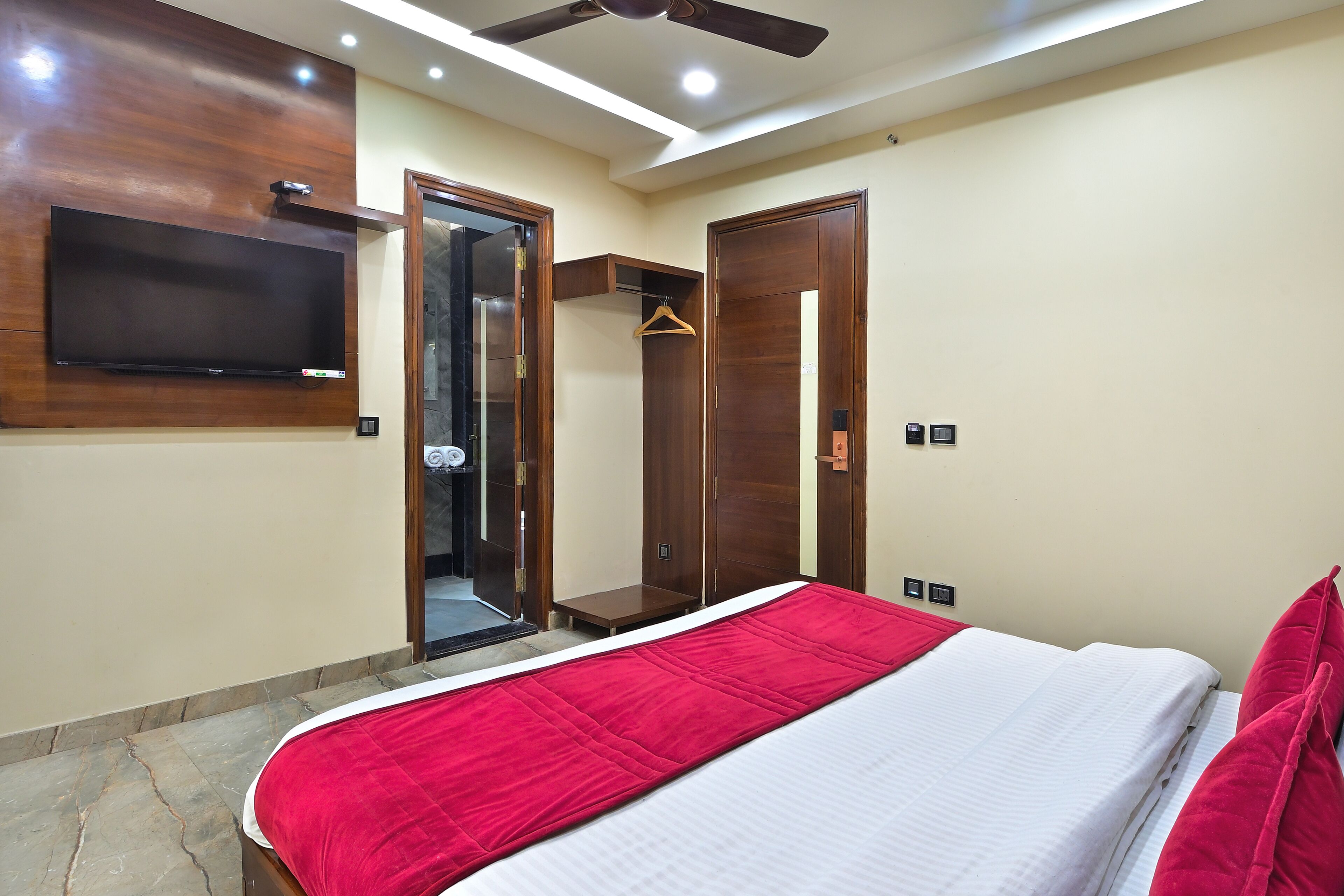 A bedroom with a bed, a TV mounted on the wall, a wardrobe, and a ceiling fan.